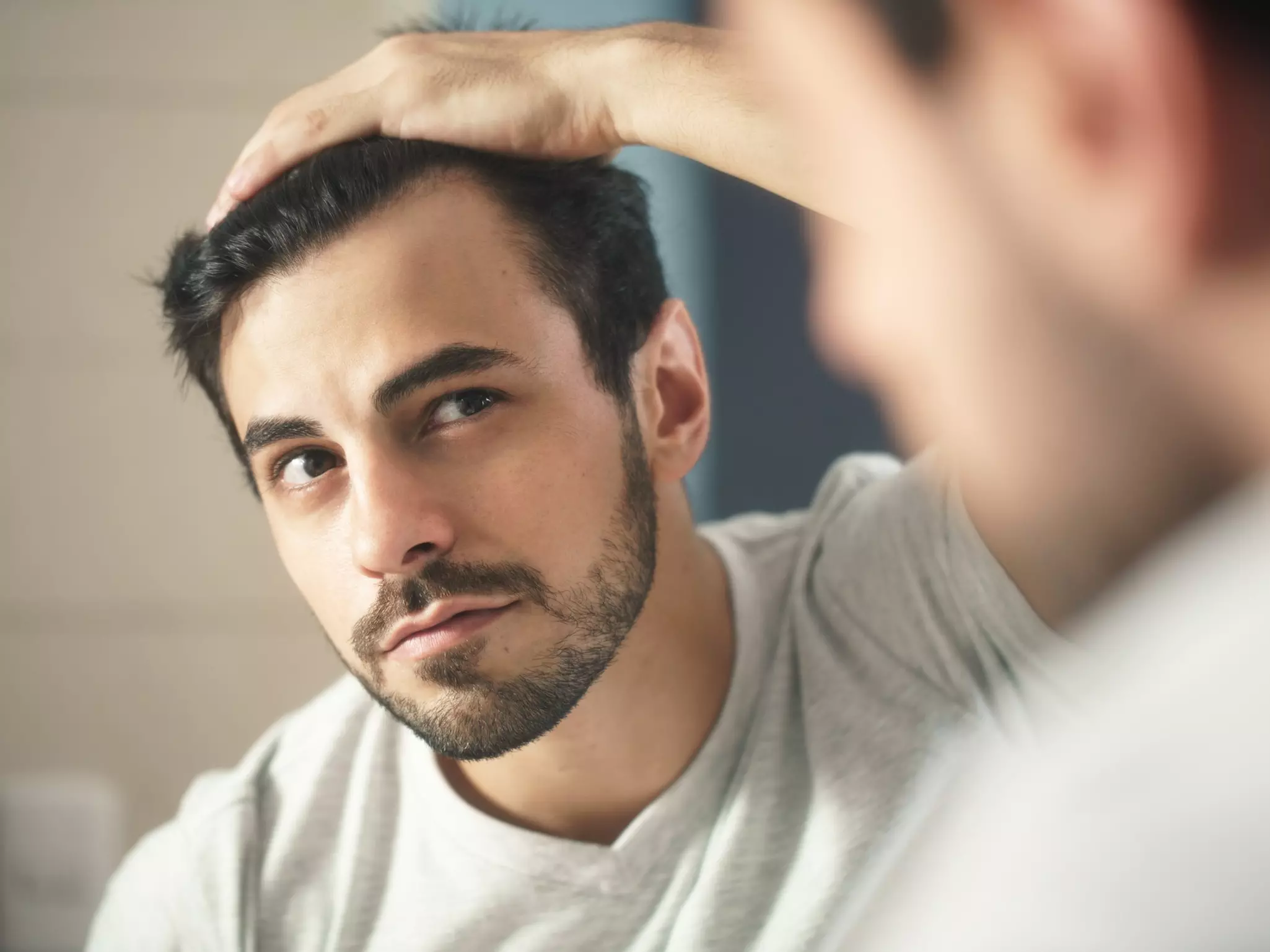 Ein junger Mann schaut kritisch in den Spiegel, um die ersten Anzeichen von erblich bedingtem Haarausfall zu erkennen