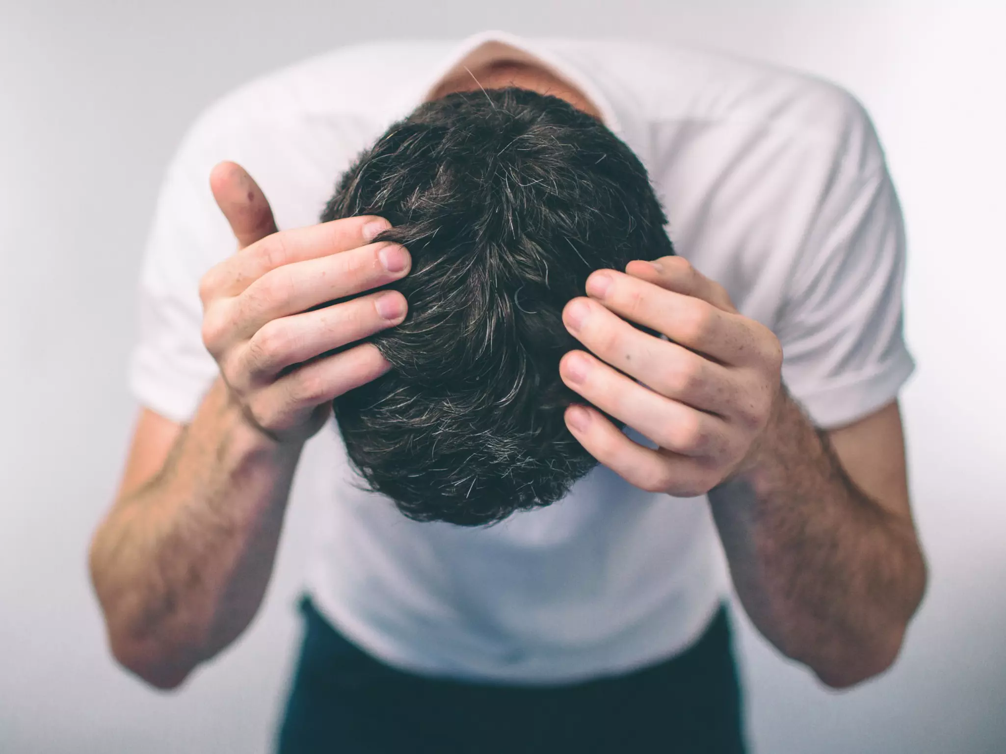 Mann mit dunklen Haaren beugt sich nach vorne und präsentiert seinen Hinterkopf als Sinnbild für Haarausfall Ursachen