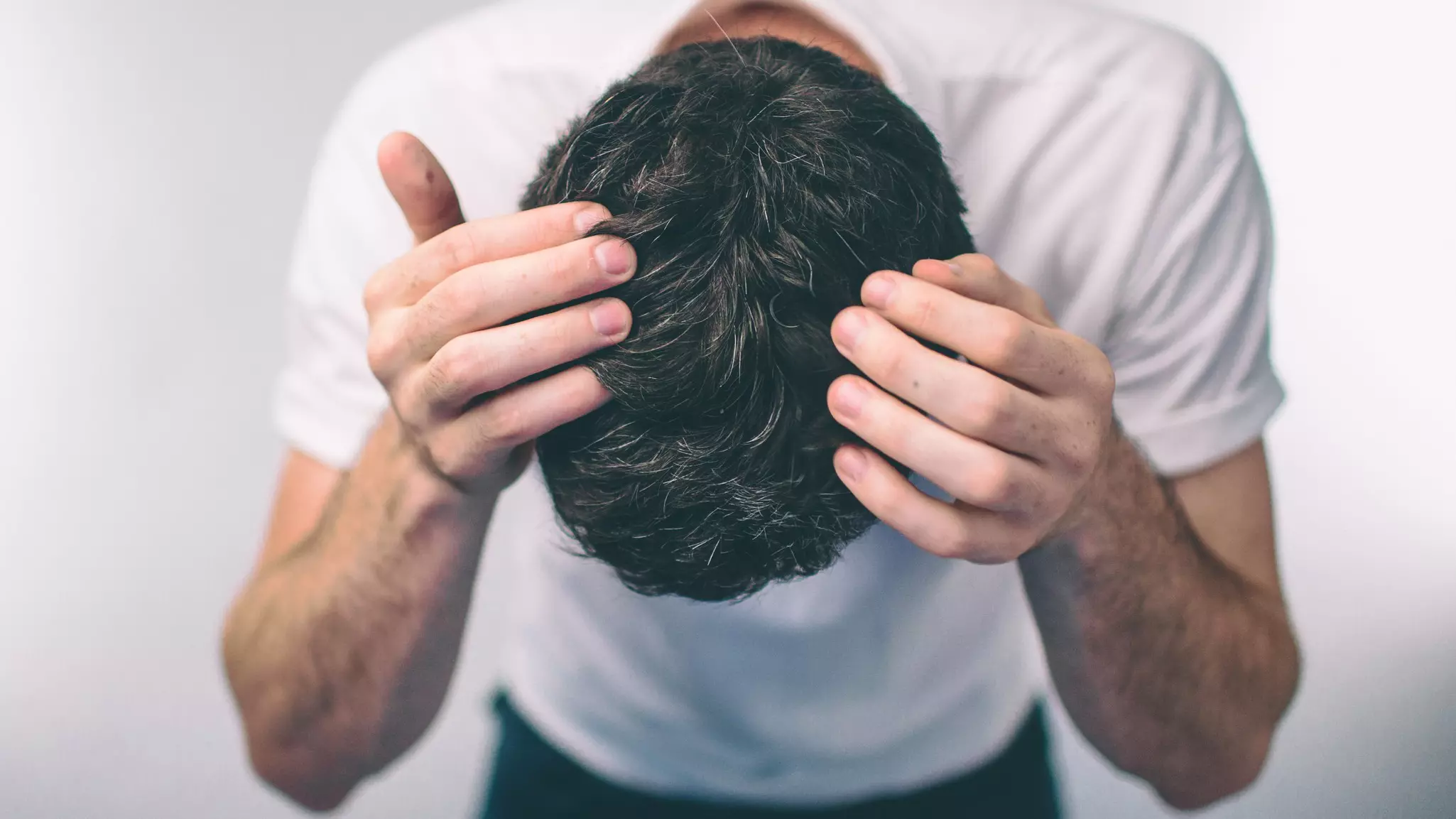 Mann mit dunklen Haaren beugt sich nach vorne und präsentiert seinen Hinterkopf als Sinnbild für Haarausfall Ursachen