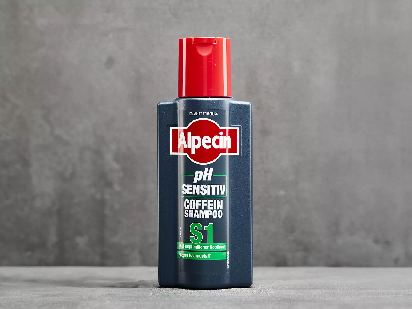 Eine graue Flasche Alpecin pH Sensitiv Shampoo S1 steht auf einer grauen Fläche, um die Aussage zu unterstützen, dass ein mildes, feuchtigkeitsspendendes Shampoo bei Juckreiz aufgrund einer empfindlichen Kopfhaut helfen kann