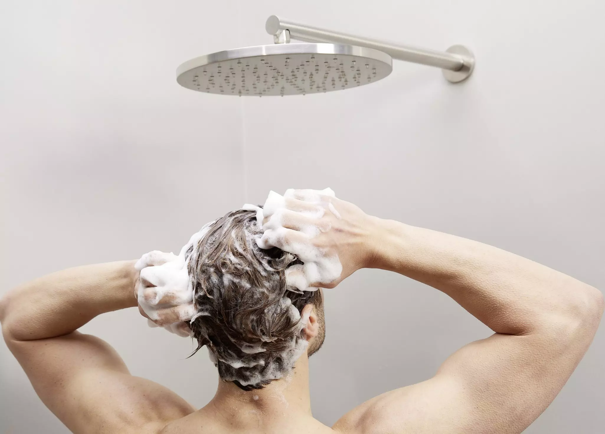Rückansicht eines Mannes unter der Dusche, der sein Haar mit einem Shampoo gegen Haarausfall wäscht