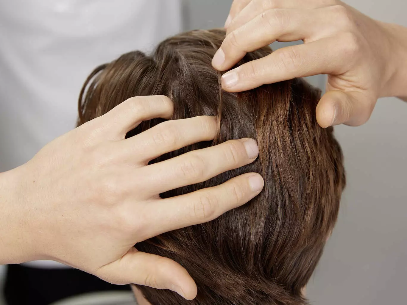 Ein Mann ertastet mit seinen Händen sein schütteres Haar am Hinterkopf und symbolisiert damit die Frage, was Männern mit Haarausfall helfen kann
