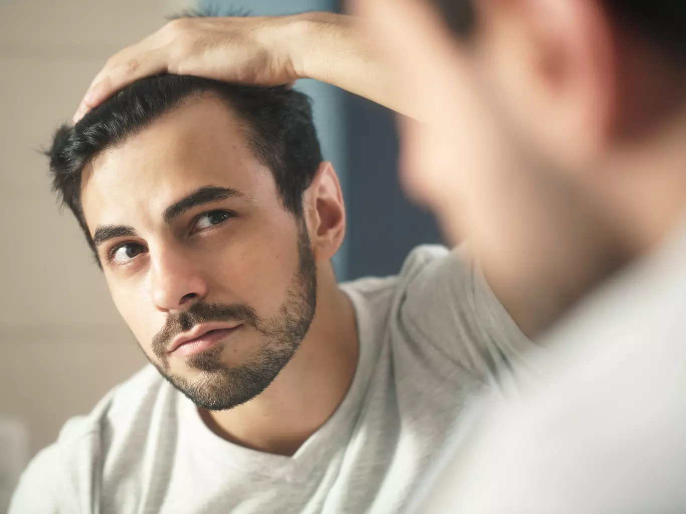 Ein junger Mann schaut kritisch in den Spiegel, um die ersten Anzeichen von erblich bedingtem Haarausfall zu erkennen
